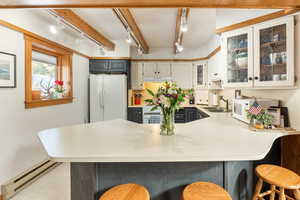 Kitchen with track lighting, a sink, a baseboard radiator, white appliances, and a peninsula