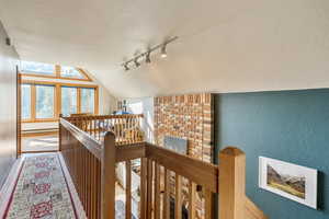 Corridor with a textured wall, an upstairs landing, baseboard heating, and lofted ceiling