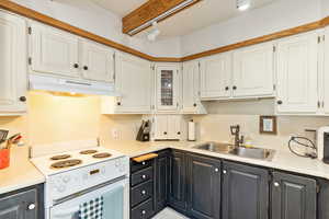 Kitchen featuring white cabinets, under cabinet range hood, light countertops, a sink, and electric stove