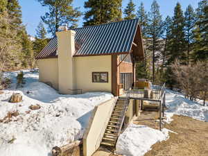 Snow covered property with stairway, metal roof, stucco siding, and a chimney