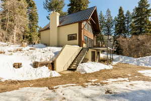 Snow covered property featuring a chimney, stairs, a wooden deck, a standing seam roof, and metal roof