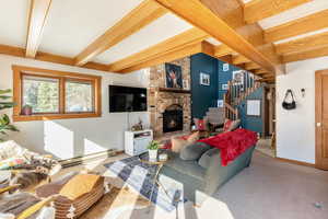 Living area featuring beamed ceiling, stairway, carpet, and a brick fireplace