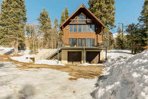 Snow covered rear of property featuring a garage and stairway