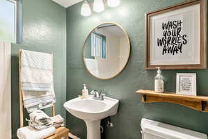 Half bath with toilet, a textured wall, and a sink