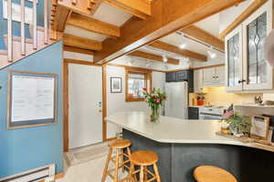 Kitchen with glass insert cabinets, white appliances, a peninsula, under cabinet range hood, and a baseboard heating unit