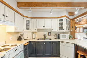 Kitchen with rail lighting, white appliances, white cabinets, under cabinet range hood, and a sink