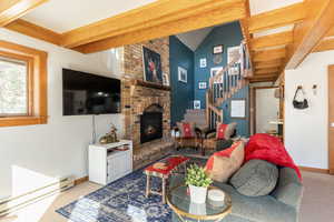 Living room with a brick fireplace, stairs, high vaulted ceiling, carpet flooring, and a baseboard heating unit