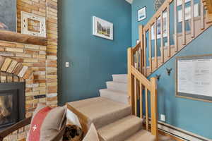 Stairs with baseboard heating and a glass covered fireplace