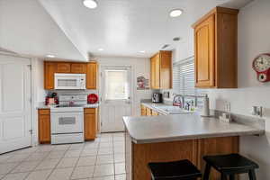 Kitchen featuring a sink, light countertops, white appliances, a peninsula, and light tile patterned flooring