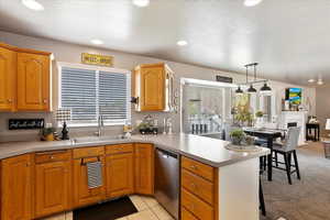 Kitchen with a peninsula, dishwasher, light countertops, a sink, and decorative light fixtures