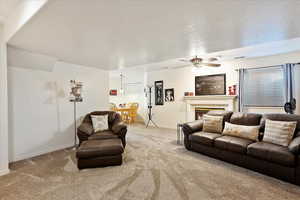 Carpeted living area with a tiled fireplace, ceiling fan, baseboards, and visible vents