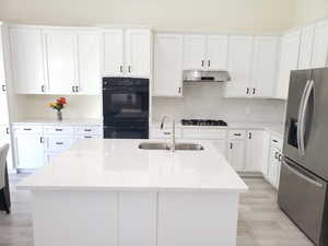 Kitchen featuring under cabinet range hood, stainless steel fridge with ice dispenser, dobule oven black, gas stovetop, and a sink