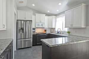 Kitchen with stainless steel fridge with ice dispenser, white microwave, lofted ceiling, black range with electric stovetop, and a sink