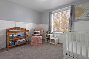 Carpeted bedroom featuring a decorative wall and wainscoting