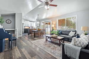 Living room featuring dark wood-type flooring, baseboards, a ceiling fan, and lofted ceiling