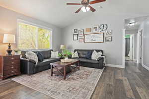 Living room featuring baseboards, dark wood-style floors, vaulted ceiling, and a ceiling fan