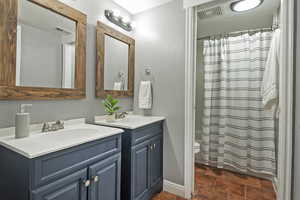 Full bathroom with a sink, visible vents, two vanities, and stone finish flooring