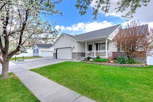 Ranch-style home featuring driveway, a front lawn, an attached garage, fence, and covered porch