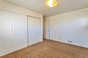 Unfurnished bedroom featuring baseboards, carpet floors, visible vents, and a closet