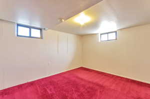 Basement featuring baseboards and dark carpet
