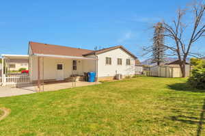 Rear view of house with a shed, an outdoor structure, a patio, a carport, and a lawn