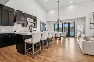 Kitchen with a kitchen breakfast bar, premium range hood, light countertops, a center island with sink, and high vaulted ceiling