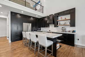 Kitchen featuring high end refrigerator, baseboards, black electric cooktop, dark cabinets, and custom range hood