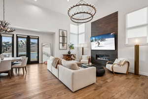 Living area with wood-type flooring, a towering ceiling, an inviting chandelier, and a glass covered fireplace