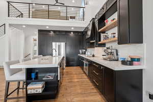 Kitchen with custom range hood, high quality fridge, light wood-style floors, and open shelves