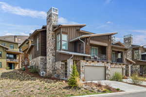 View of front facade featuring stone siding, driveway, board and batten siding, and a chimney