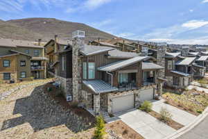 Exterior space featuring an attached garage, stone siding, metal roof, a residential view, and driveway