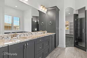 Full bathroom with a shower stall, wood finished floors, double vanity, and a sink