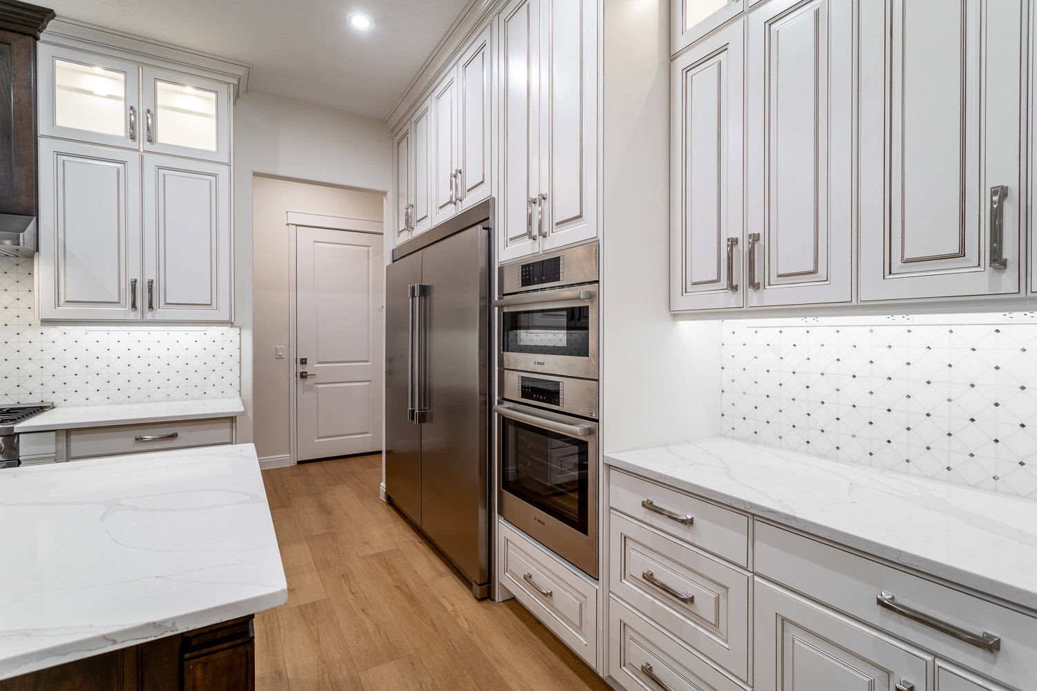 Kitchen featuring light stone counters, glass insert cabinets, decorative backsplash, light wood finished floors, and appliances with stainless steel finishes
