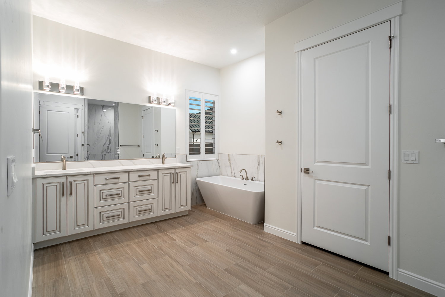 Full bath with a sink, double vanity, a freestanding tub, and wood finished floors