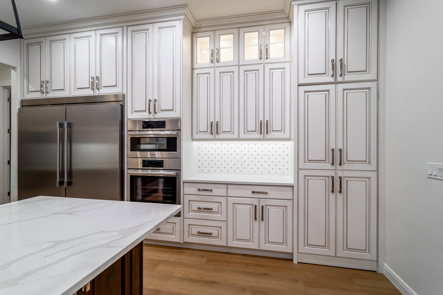 Kitchen featuring light wood-style floors, glass insert cabinets, appliances with stainless steel finishes, light stone counters, and backsplash