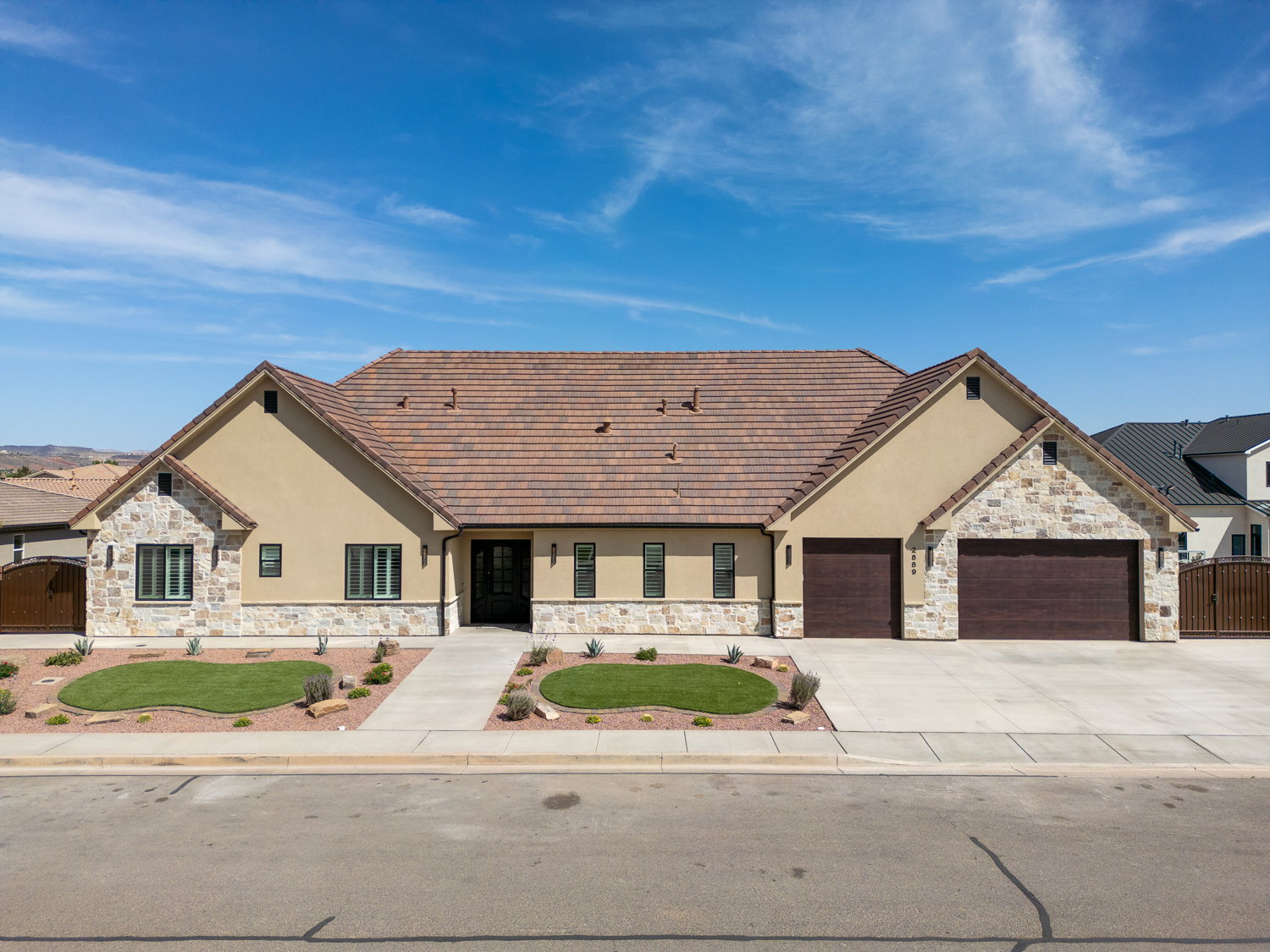 Ranch-style house with stucco siding, driveway, stone siding, an attached garage, and a gate