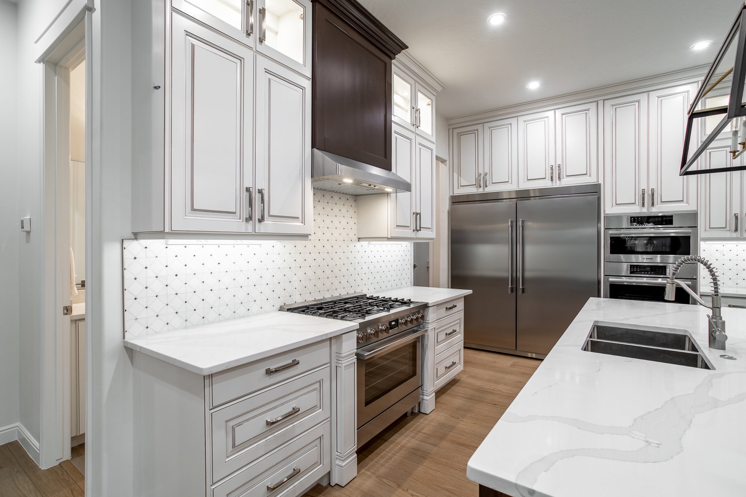 Kitchen featuring glass insert cabinets, wall chimney exhaust hood, a sink, light wood-style floors, and high end appliances
