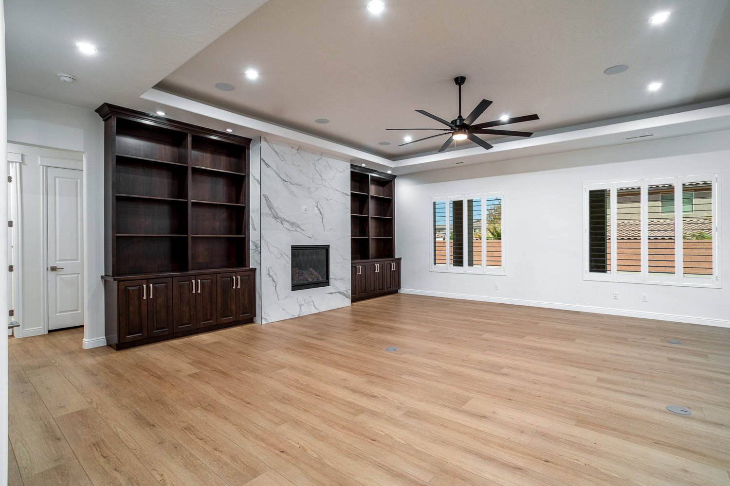 Unfurnished living room with a raised ceiling, light wood finished floors, a ceiling fan, and built in shelves
