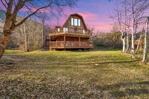 Front of south facing house at dusk featuring a deck, a gambrel roof, and a lawn.