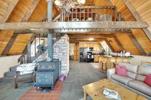 Living area featuring wood ceiling, a wood stove, lofted ceiling with beams, and a notable chandelier