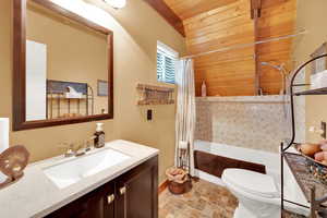 Full bathroom with vanity, toilet, wood ceiling, wood walls, and shower / tub combo with curtain