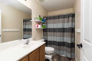 Bathroom with vanity, a shower with curtain, toilet, visible vents, and wood finished floors
