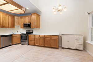 Kitchen featuring a notable chandelier, light wood-style flooring, light countertops, decorative light fixtures, and appliances with stainless steel finishes