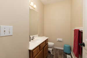 Half bath with vanity, visible vents, toilet, wood finished floors, and baseboards