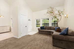 Carpeted living area with a chandelier, high vaulted ceiling, and baseboards