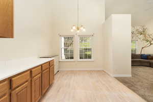 Unfurnished dining area with light wood-type flooring, a notable chandelier, a high ceiling, and baseboards