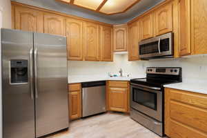 Kitchen featuring light wood-style floors, brown cabinetry, a sink, light countertops, and stainless steel appliances