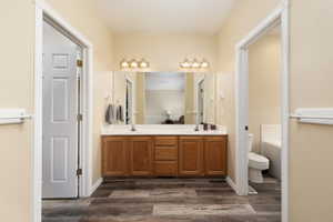 Bathroom with a sink, toilet, double vanity, and wood finished floors