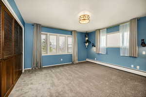 Unfurnished bedroom with a closet, carpet, a baseboard heating unit, and baseboards