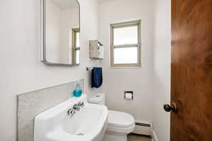 Half bathroom with baseboard heating, a sink, baseboards, and toilet